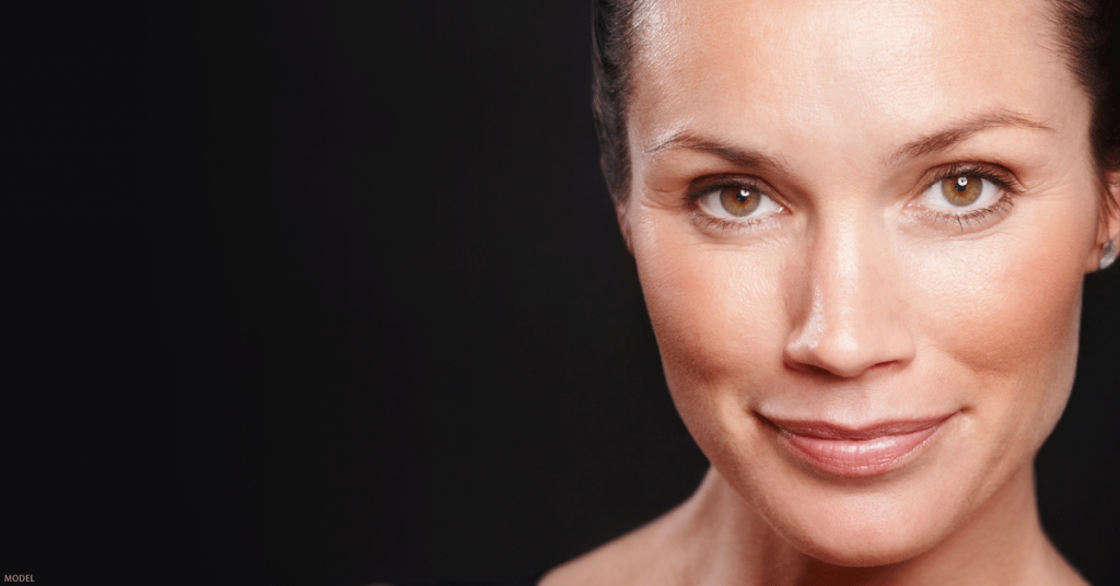 High-contrast portrait of attractive woman in her 40s with hair pulled back against black background