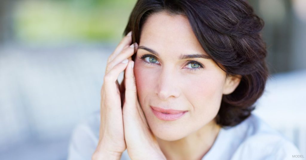 A woman smiling with their hands on their face. (Model)