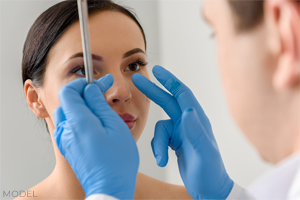 Surgeon with gloved hands assessing patient's facial features at consultation