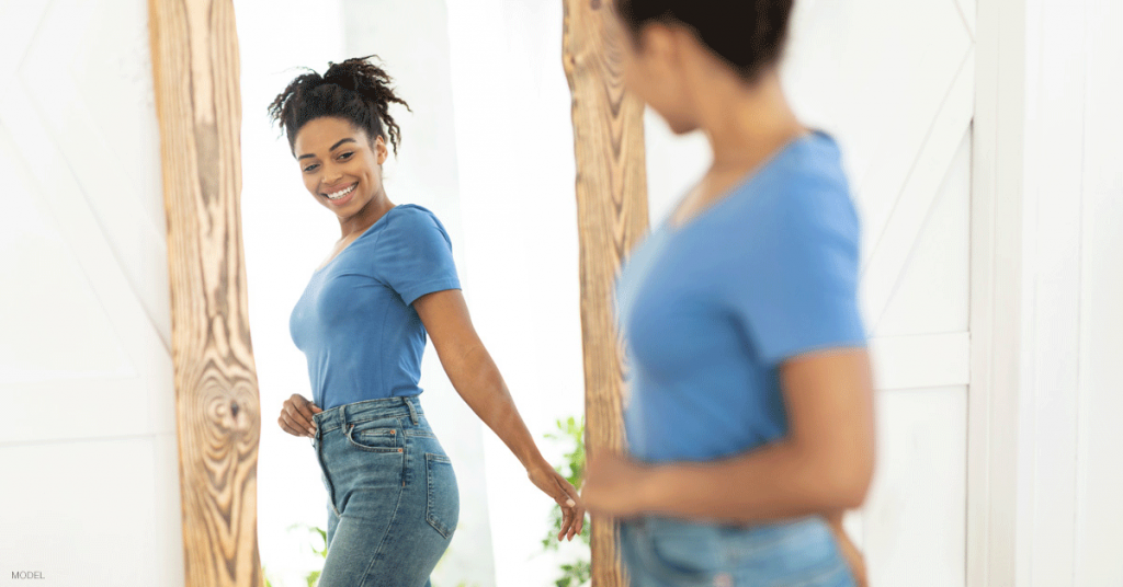 Woman in Boston, MA admiring her tummy tuck results in the mirror