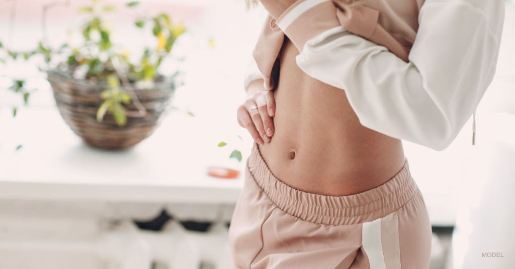 A close up of a woman's flat tummy as she lifts her shirt. (Model)